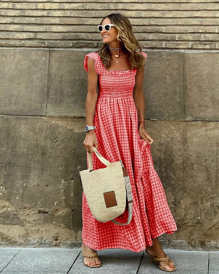 Woman model styling a spring gingham maxi dress against a cement wall background.