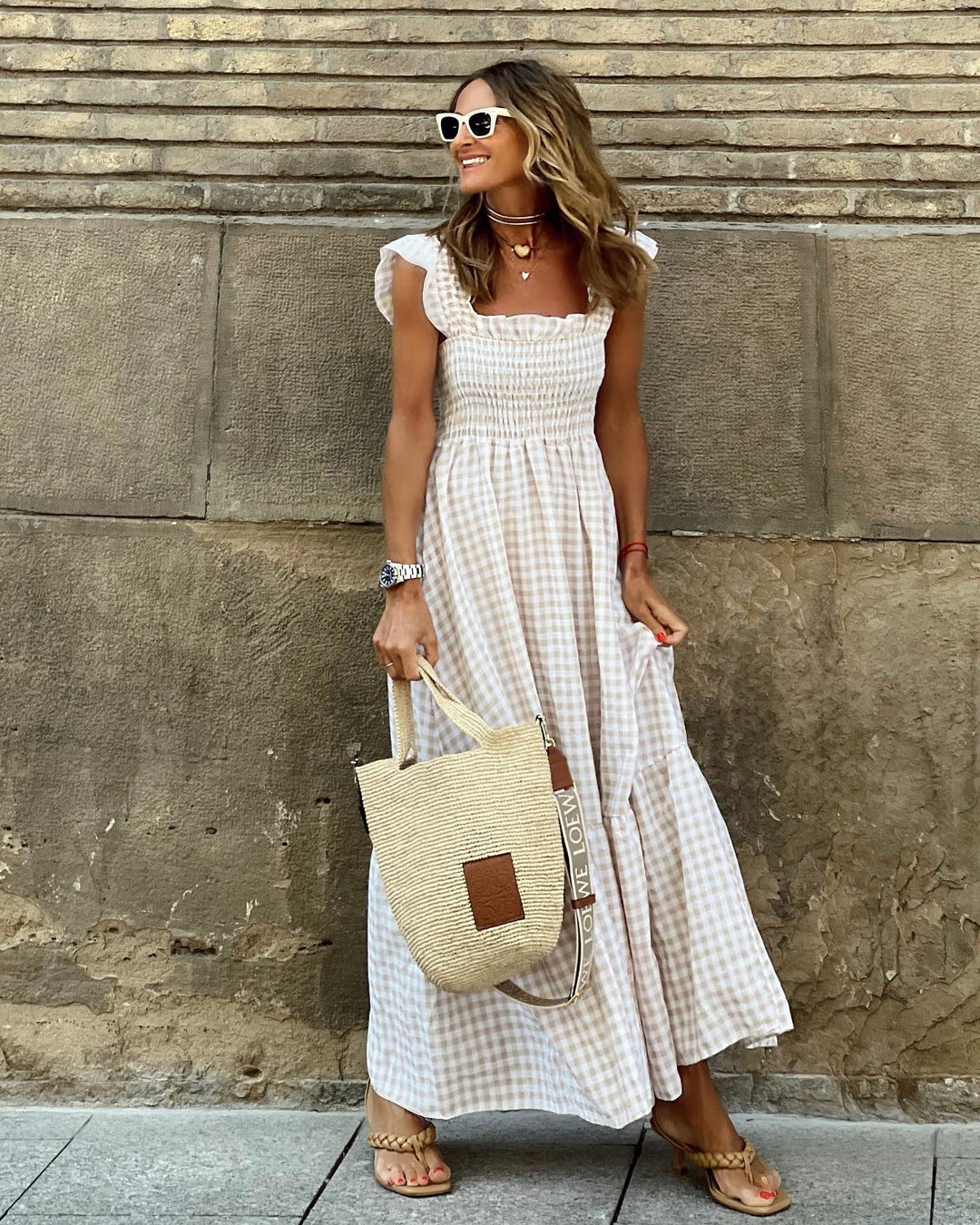 Woman model wearing a gingham maxi dress against a plain wall background.