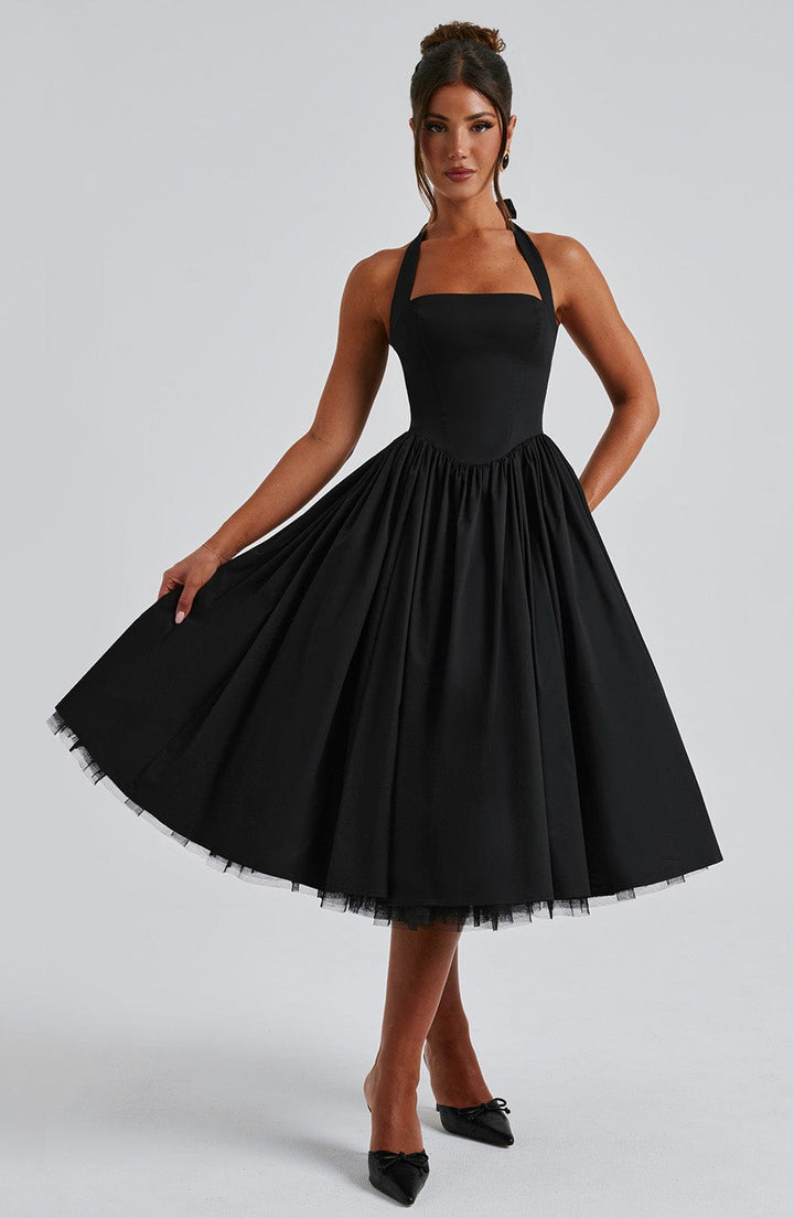 Woman modeling sleeveless party dress with flared skirt, gray backdrop.