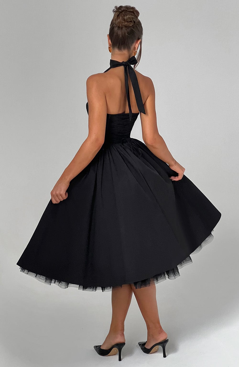 Female model showing dress movement on gray plain studio background, back view