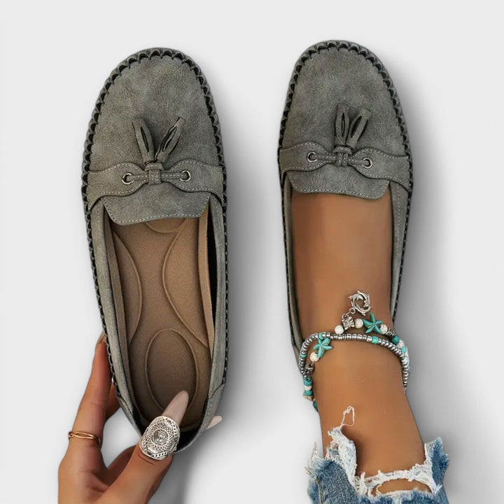 Gray loafers with tassels worn on a white background