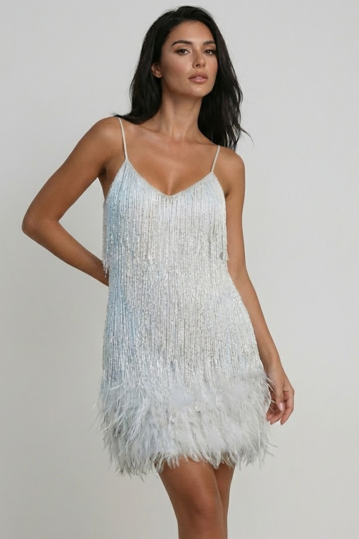 Female model in a beige mini dress with feather-style hem detail on a plain background.
