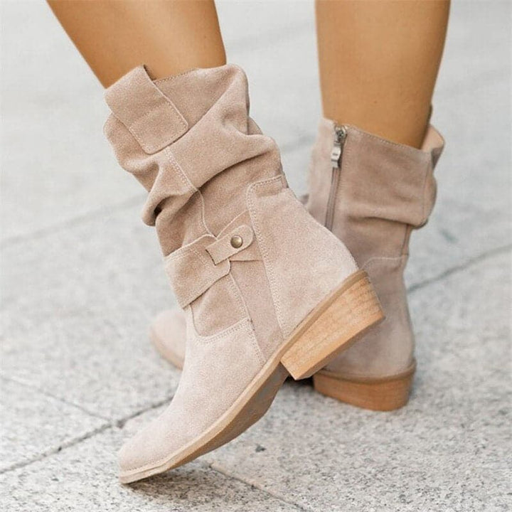 Beige boots with a button detail on a light gray pavement background