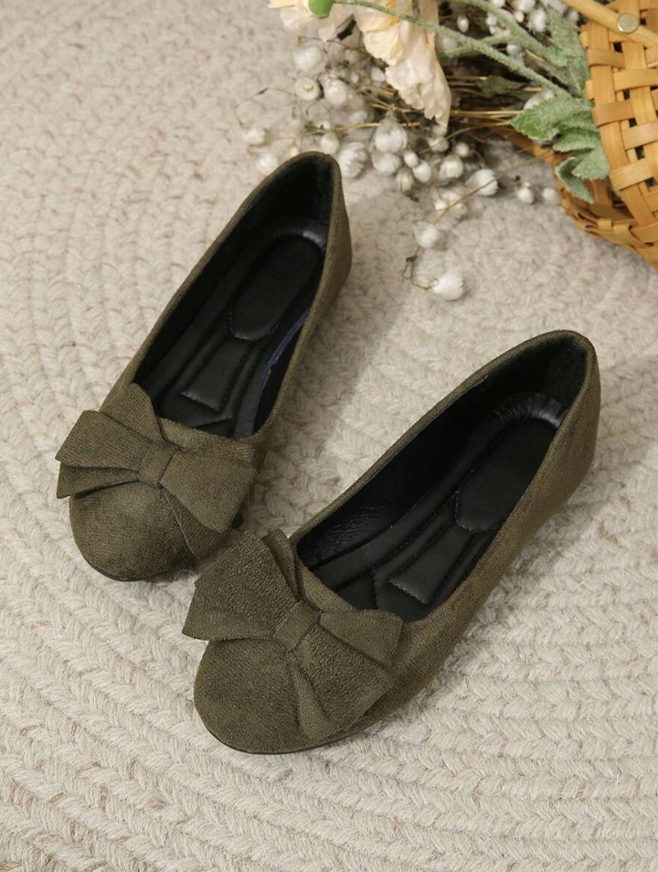 Pair of green flat shoes with bow details on a textured surface.