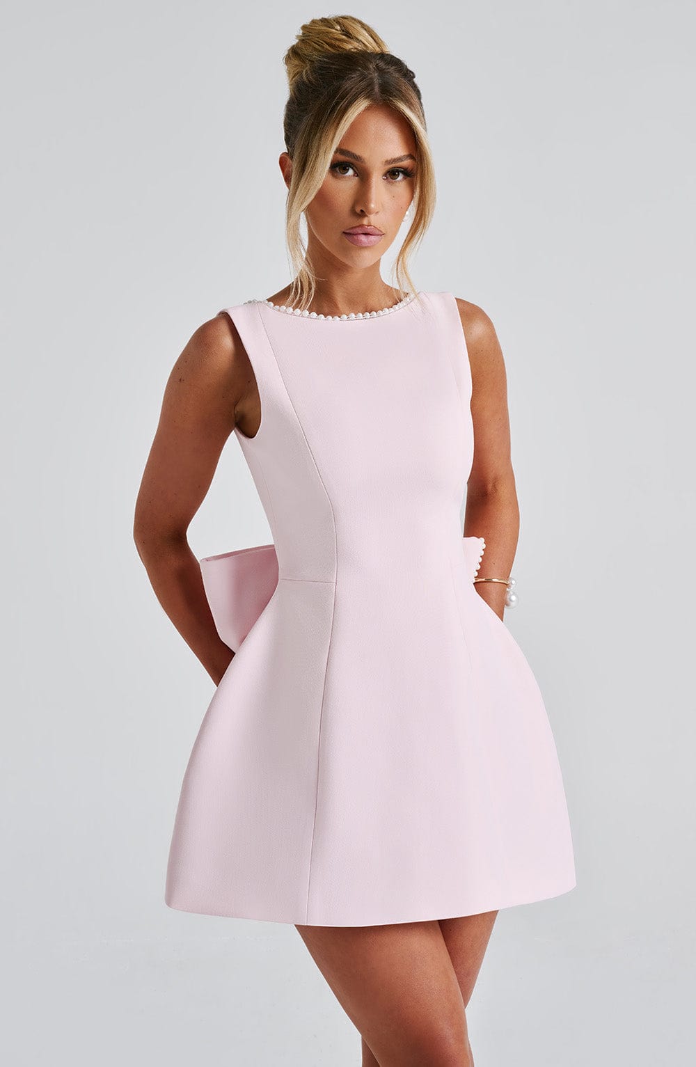 Woman showcasing a tailored mini dress with a clean silhouette on a plain background.