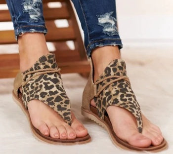 Relaxed foot pose wearing sandals on clean beige background.