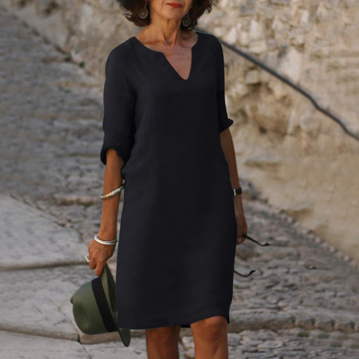Model wearing a simple midi dress with light sleeve coverage against a plain background.