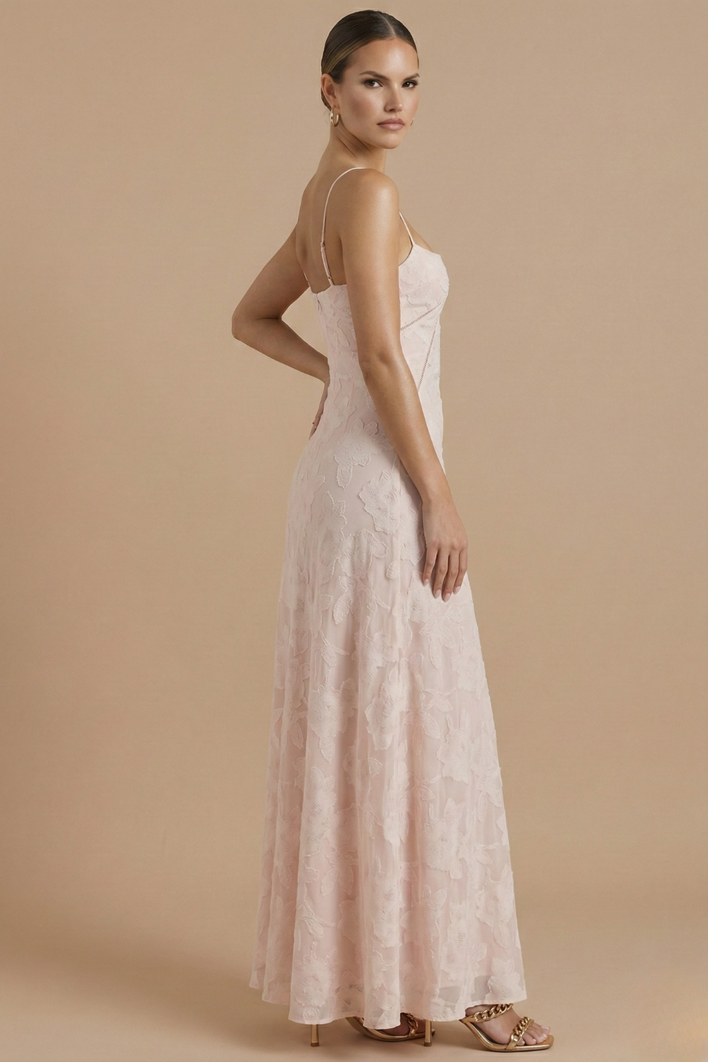  Female model showcasing a floral evening dress with thin straps on a plain background.