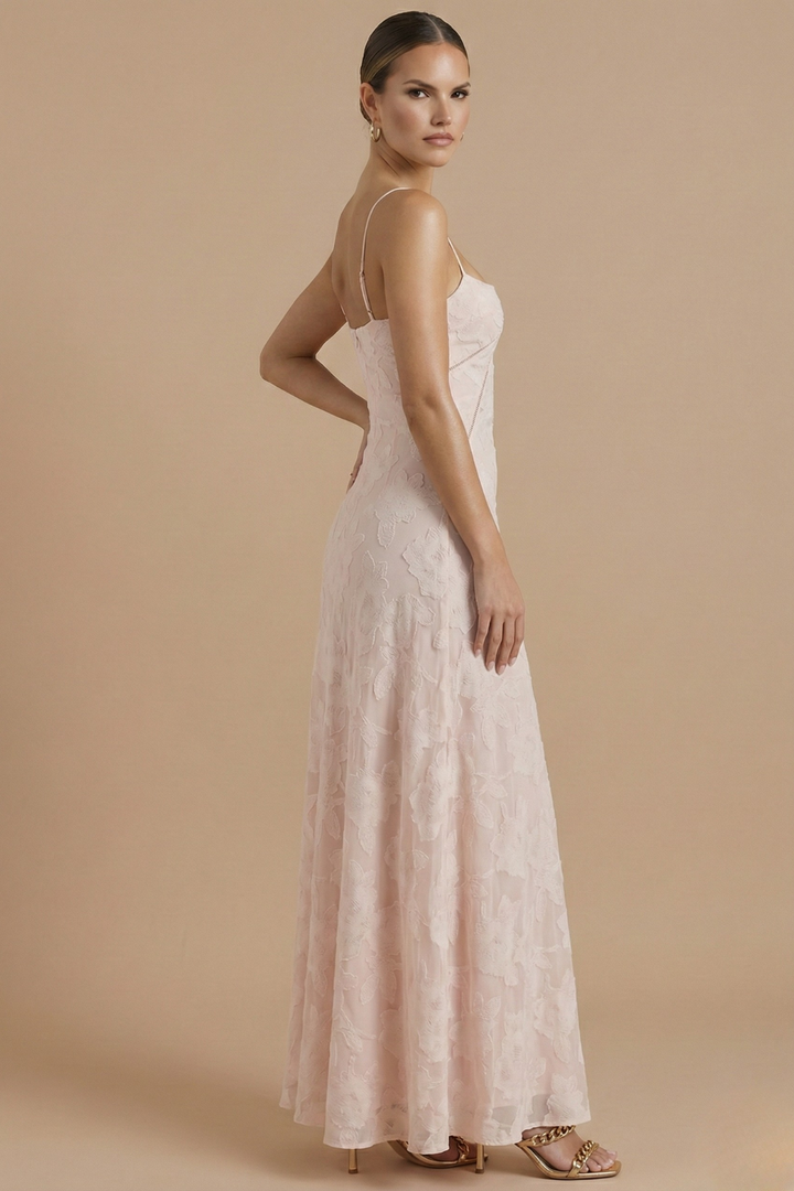  Female model showcasing a floral evening dress with thin straps on a plain background.