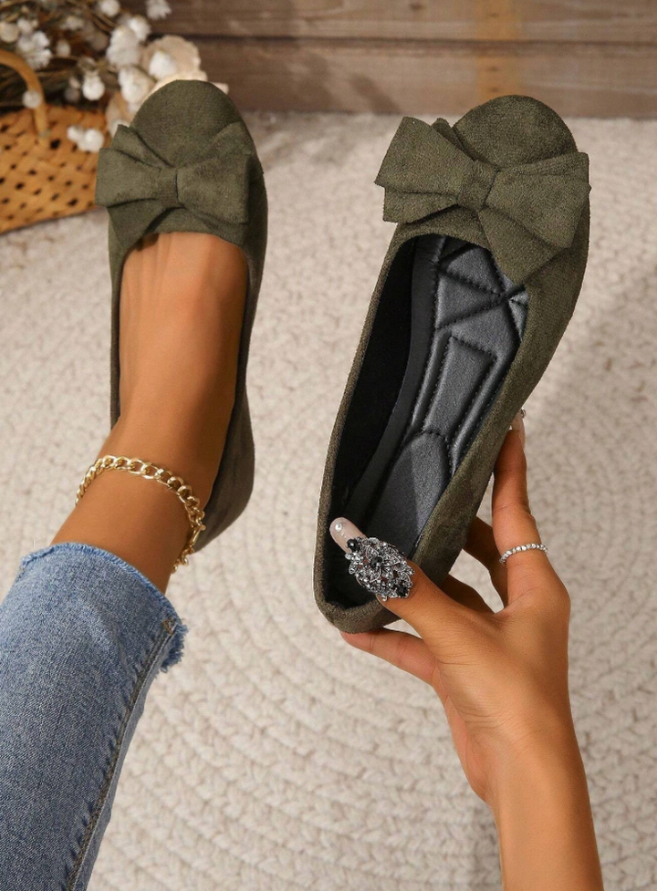 Green flat shoes with a bow held by a hand on a textured surface.