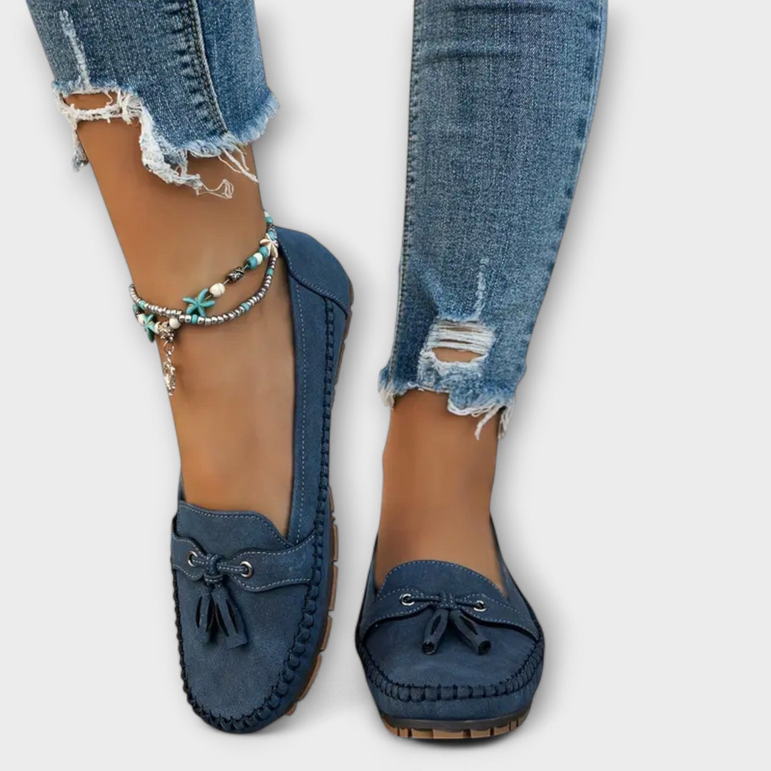 Blue loafers worn with ripped jeans on a white background