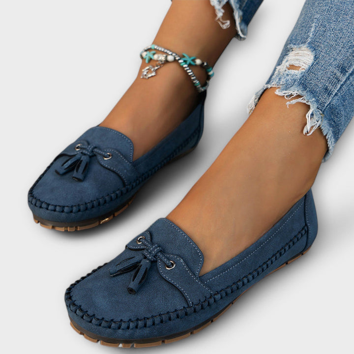Blue loafers worn with ripped jeans on a white background