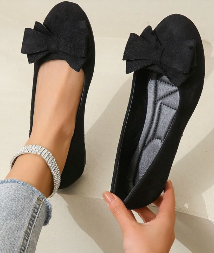 Black flats with bow detail worn by a person on a light background