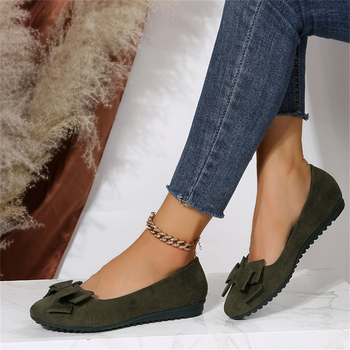 Green loafers worn with blue jeans on a white surface.
