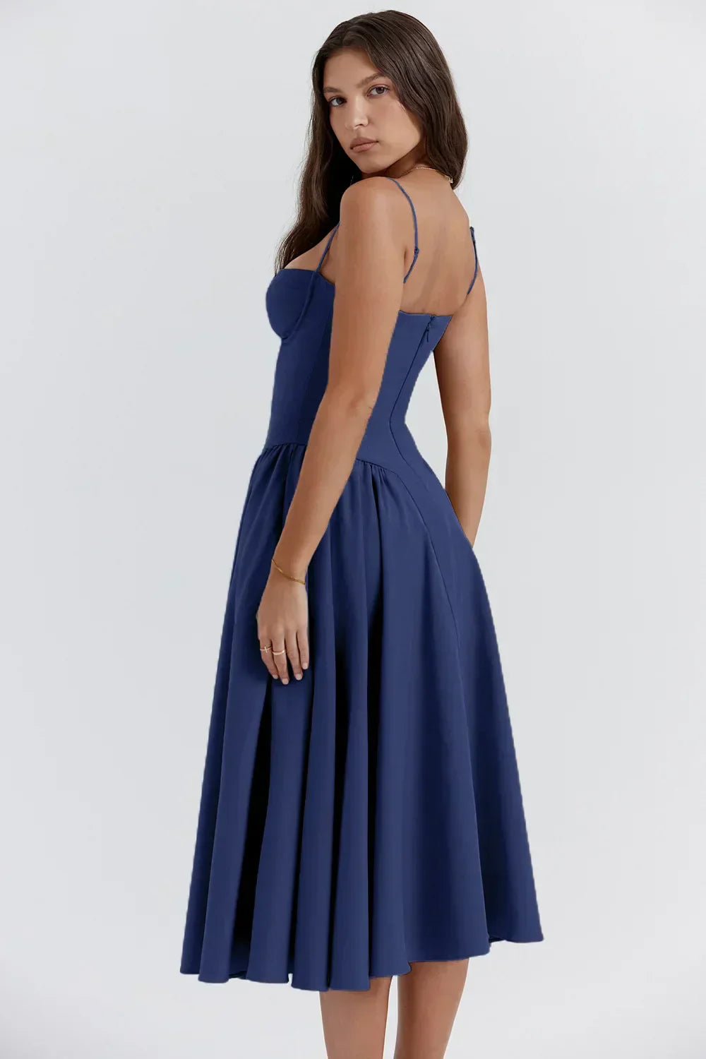 Woman showcasing a soft flowy dress with delicate straps on a plain background