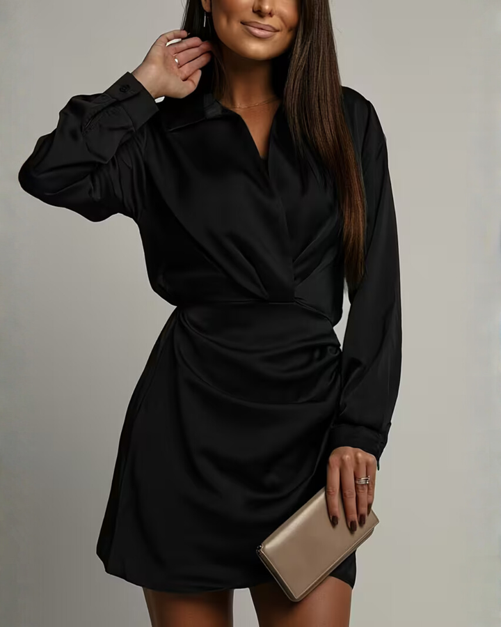Female model wearing a long sleeve mini dress with soft drape on a plain background.