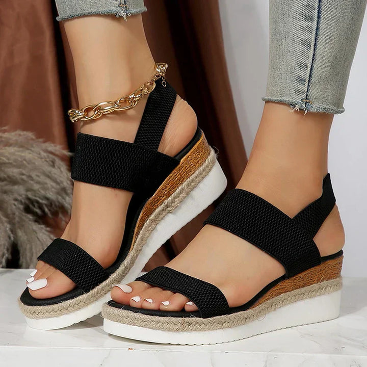 Foot model showing elastic strap sandals on clean white floor.