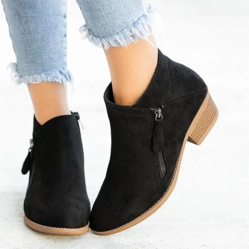 Black ankle boots with a brown sole worn with light blue jeans on a white background
