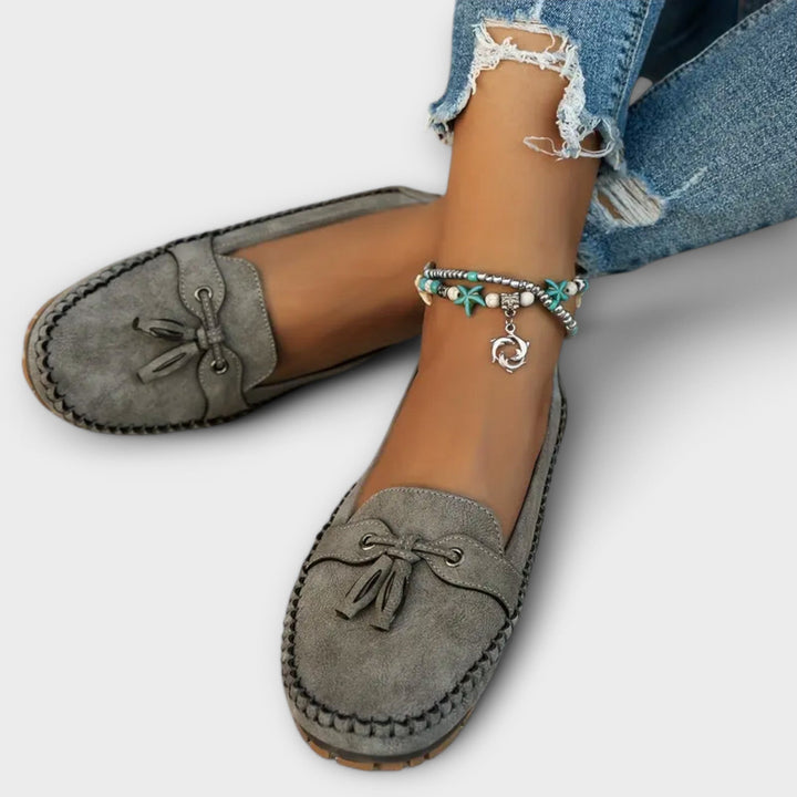 Gray loafers worn with ripped jeans and a anklet on a light background