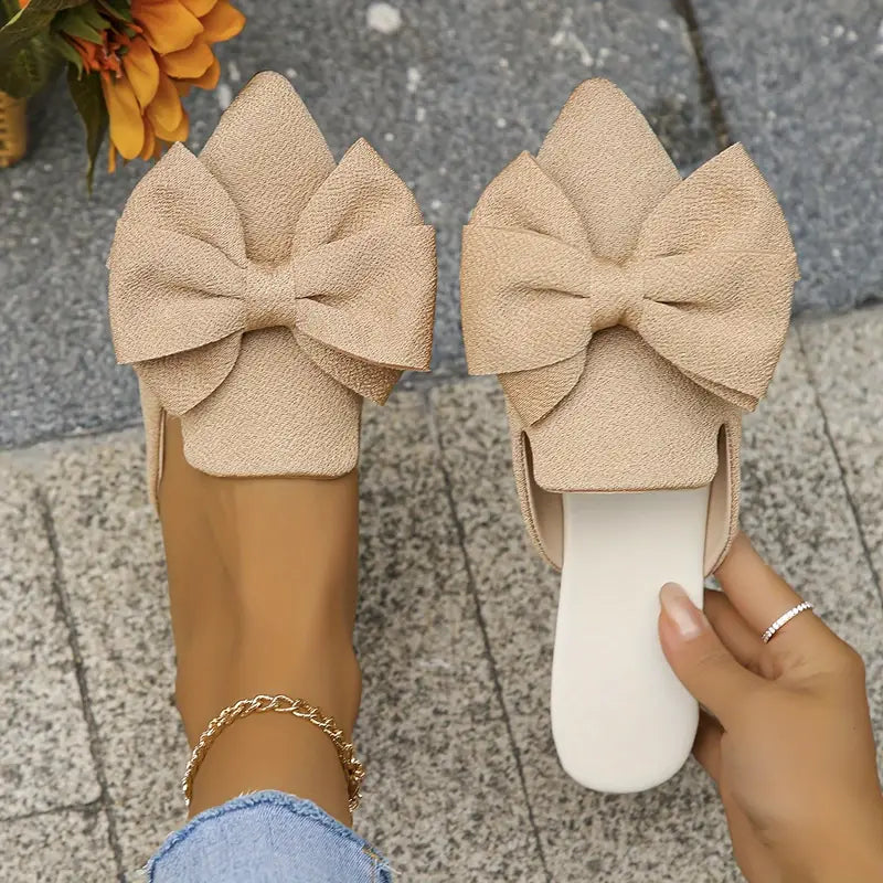 Side view of pointed toe mules on beige tile background