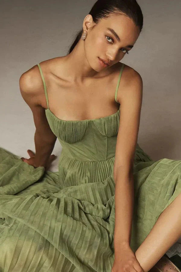 Woman sitting wearing a feminine pleated midi dress with delicate straps on a clean background.