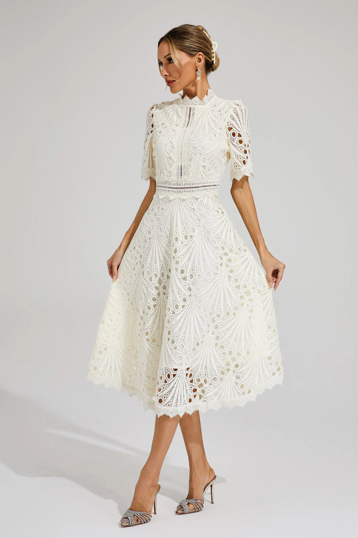 Woman model in a chic lace dress with short sleeves and fit and flare shape on a plain background.