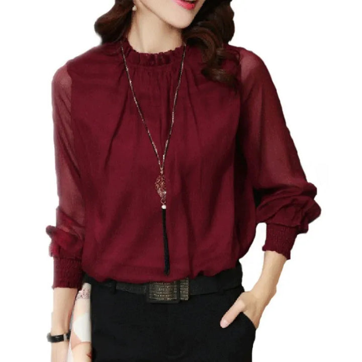 Female model wearing a flowing ruffle blouse on a plain background.