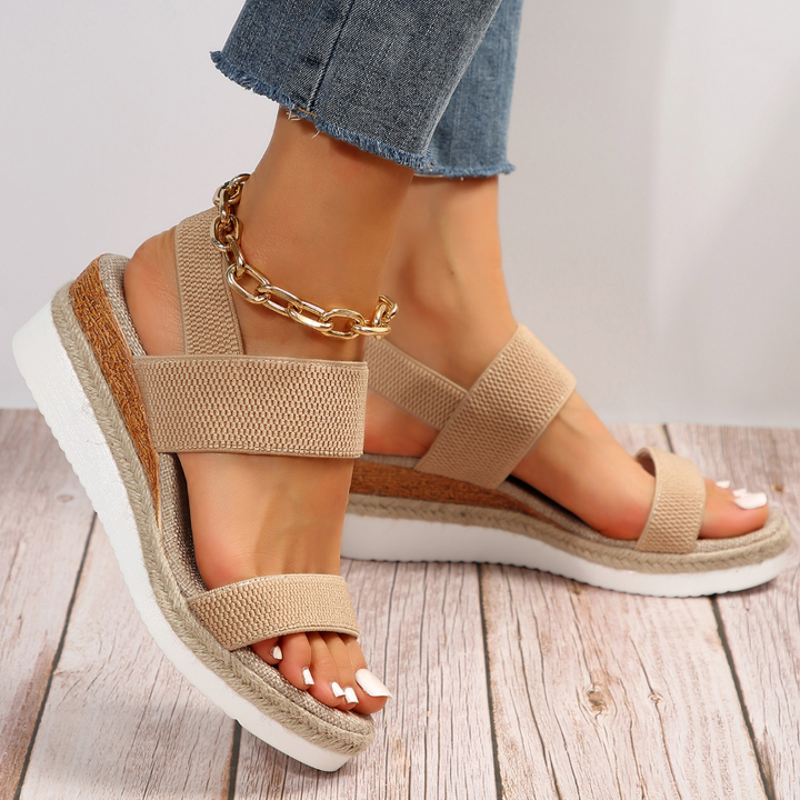 Foot model wearing platform sandals on gray floor side angle.