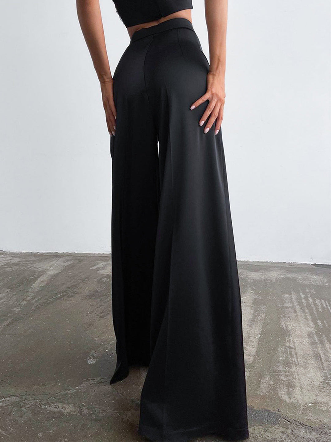 Female model standing in smooth long pants with a plain backdrop.