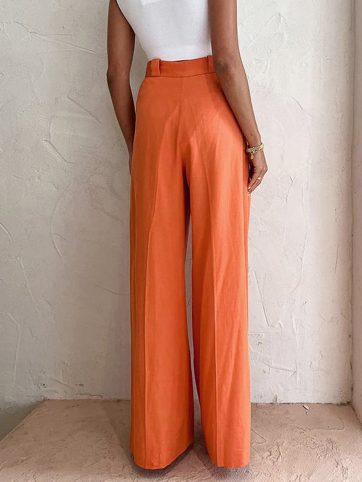 Woman styled in casual thin long pants with a plain backdrop.
