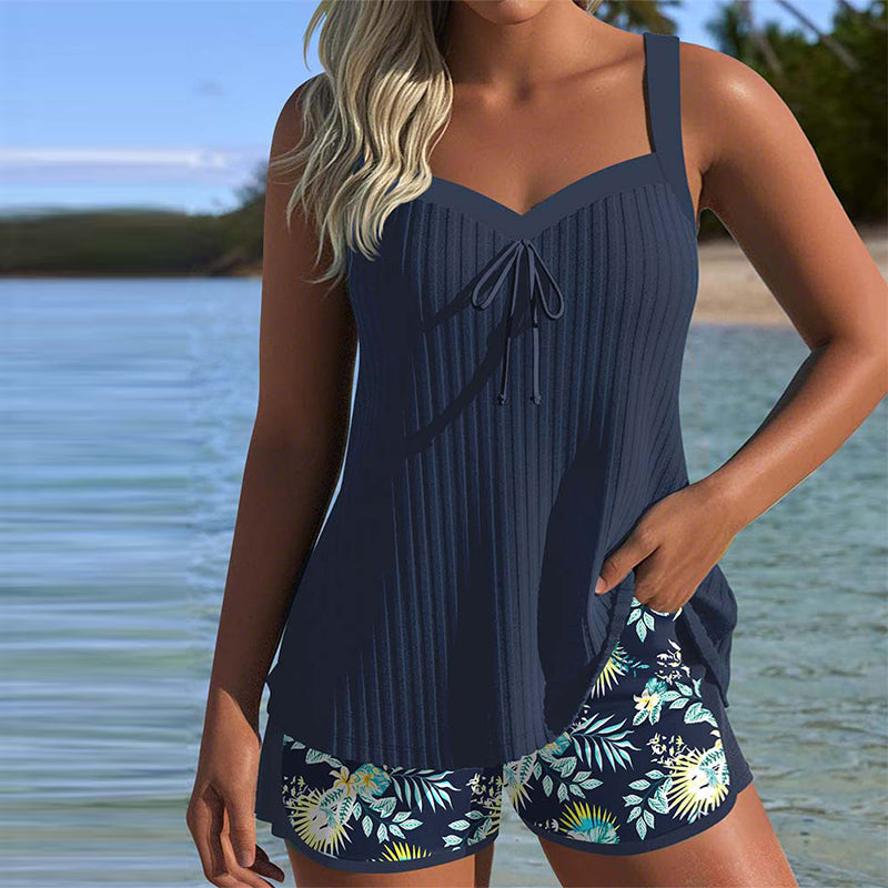 Female model wearing a striped tankini swimsuit with beach shorts on a plain background.
