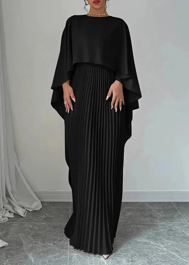 Woman in a graceful maxi dress with cape-style detail against a plain background.