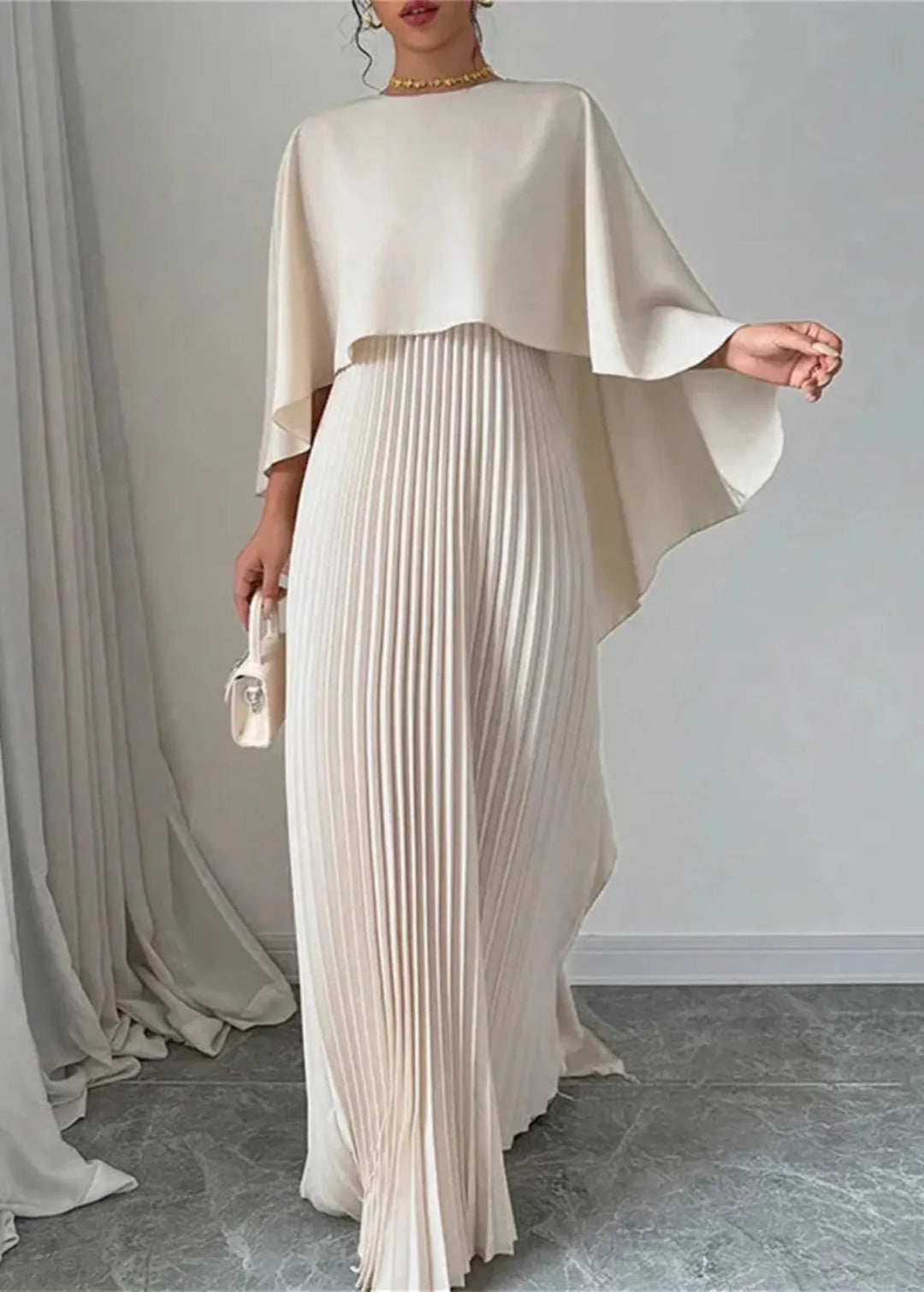 Female model wearing a pleated cape maxi dress against a plain background.