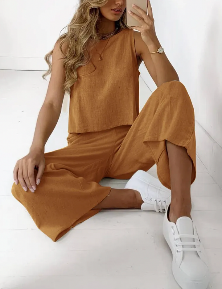 Female model wearing a stylish sleeveless top and wide trousers set on a plain background.