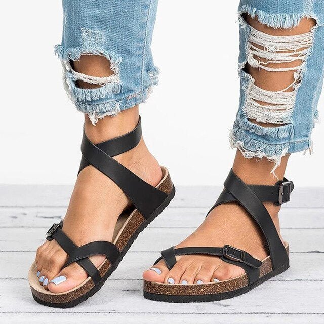 Female model standing in strappy everyday sandals on a plain background.