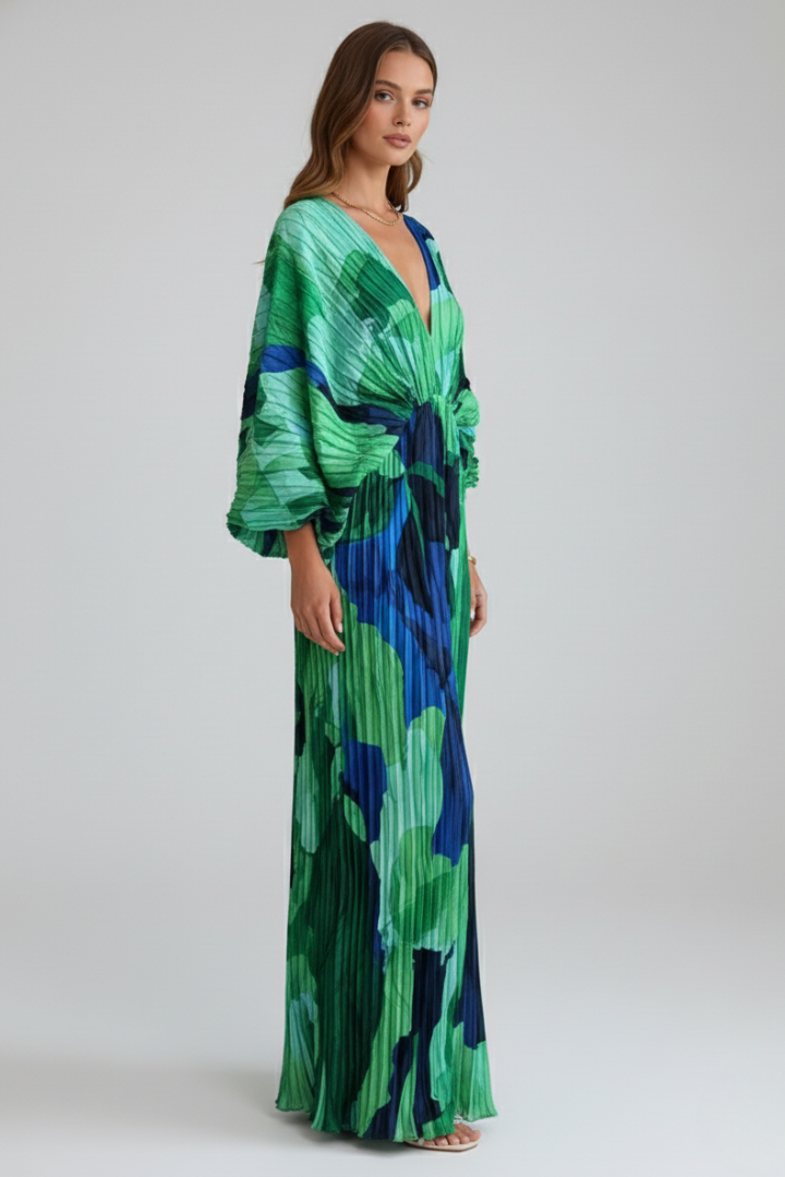 Woman posing in flowing pleated dress against plain gray background.