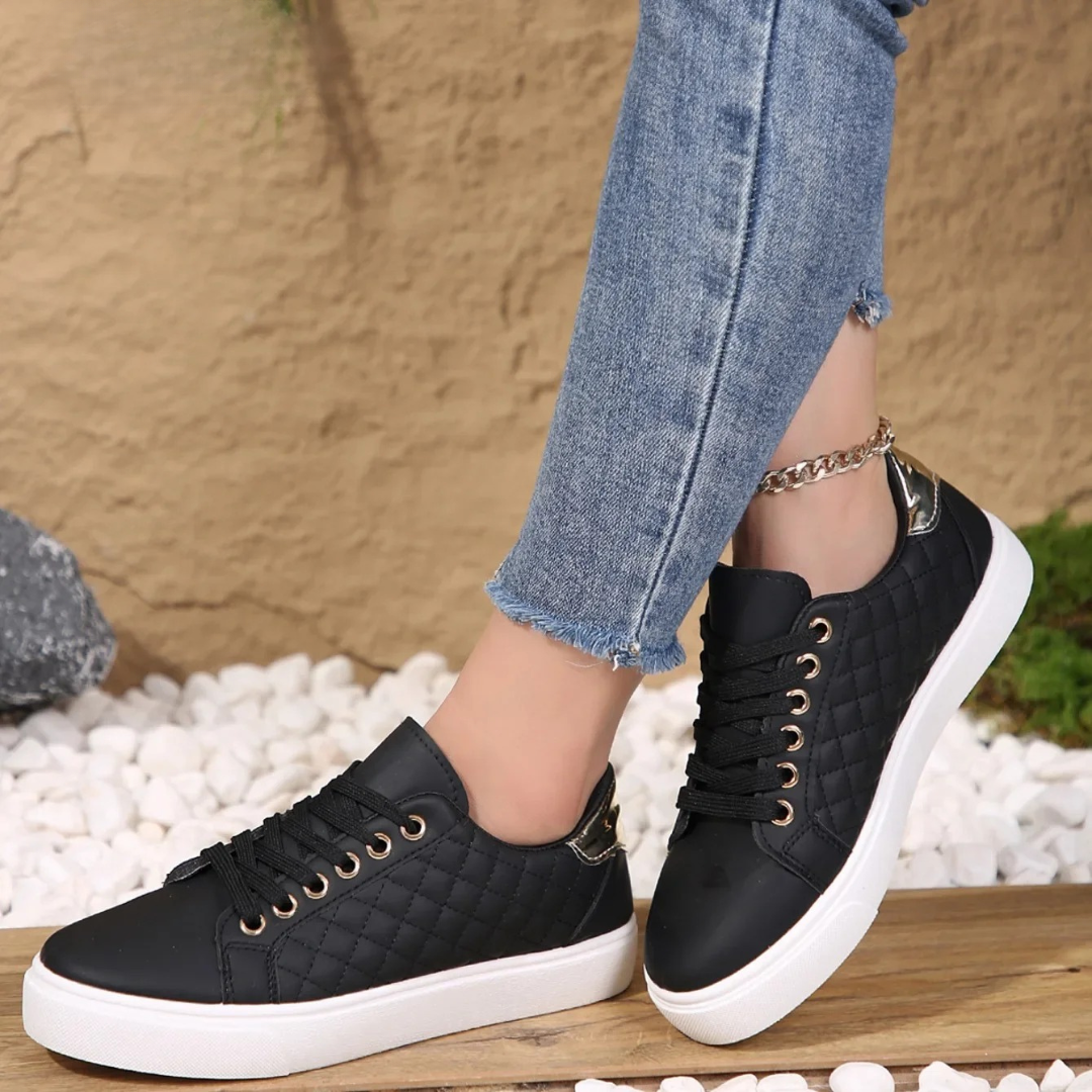 Black sneakers with white soles worn with blue jeans against a textured wall background