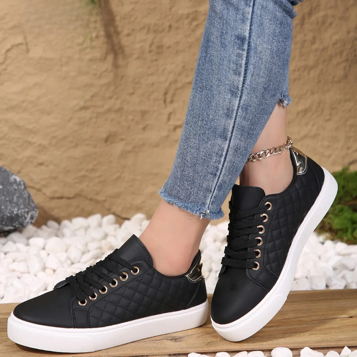 Black sneakers with white soles worn with blue jeans against a textured wall background