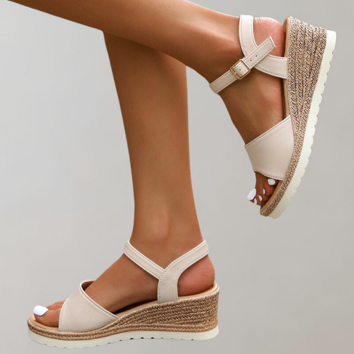 Woman standing in open-toe wedge sandals with a plain background