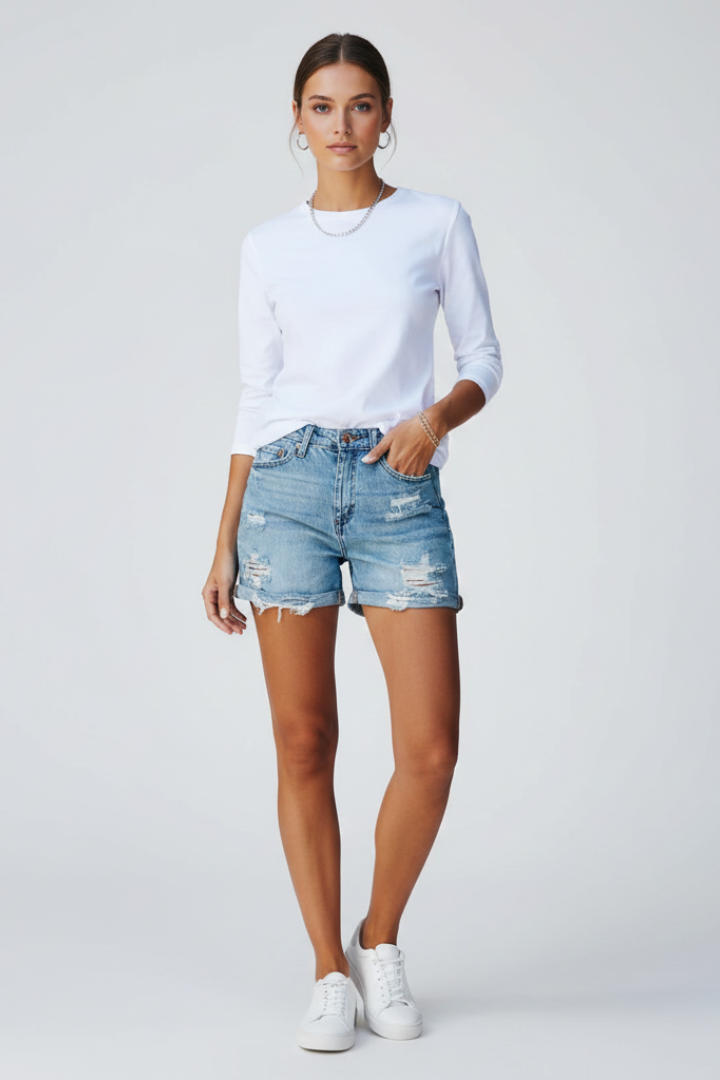 Female model wearing ripped denim shorts with white long sleeve top in front view