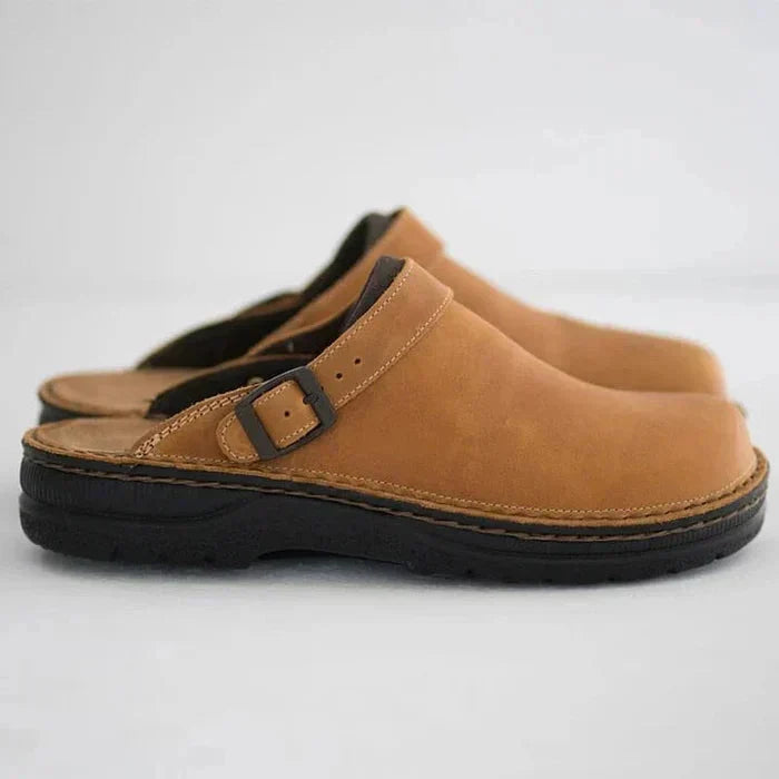 Pair of brown clogs with a buckle on a light gray background