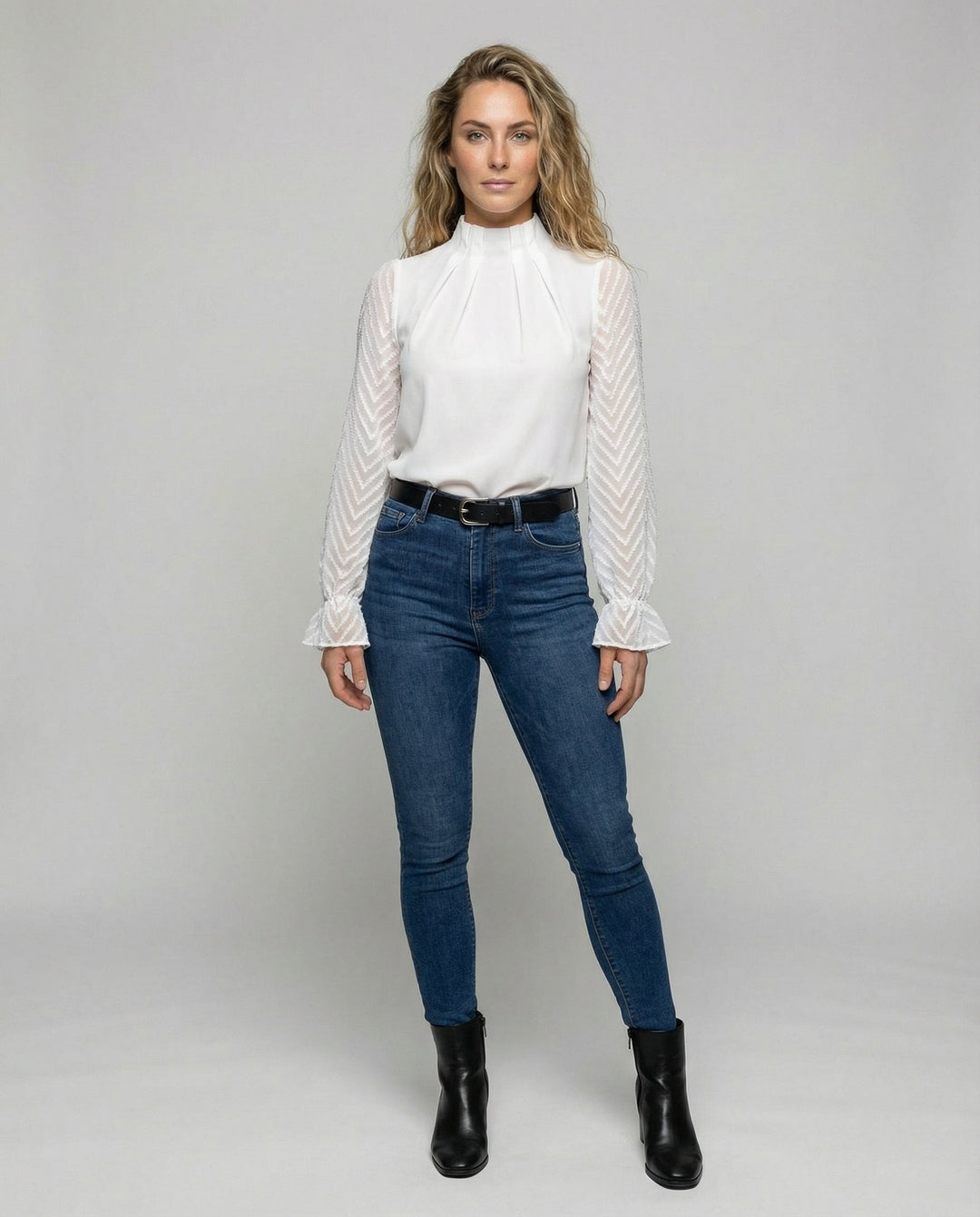 Woman showcasing a stylish long sleeve top with a classic design on a plain background.
