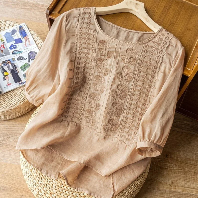 Women’s embroidered blouse with cuffed sleeves displayed on hanger against a plain background.