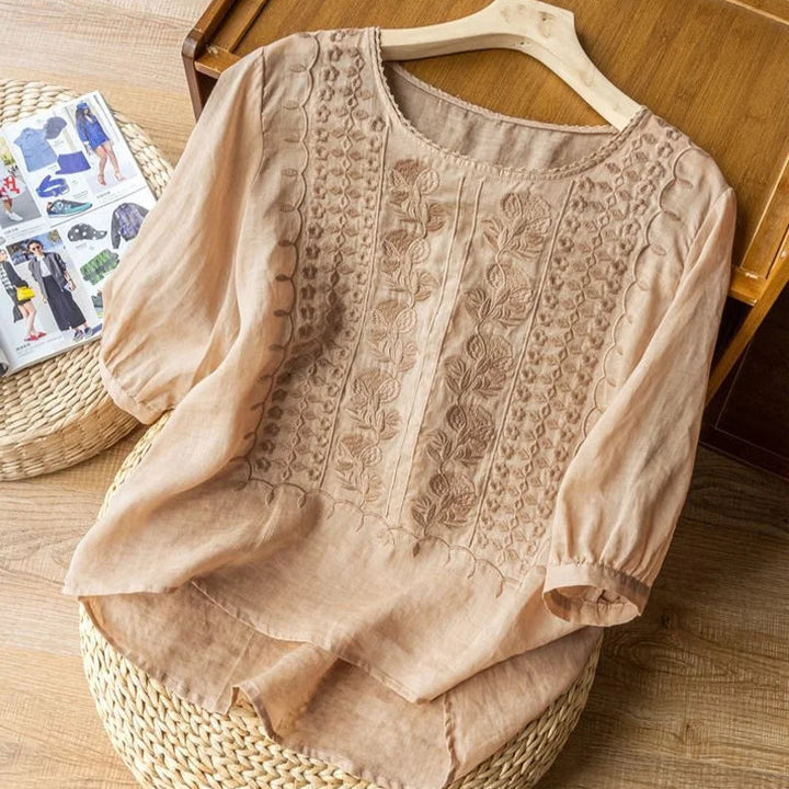 Women’s embroidered blouse with cuffed sleeves displayed on hanger against a plain background.