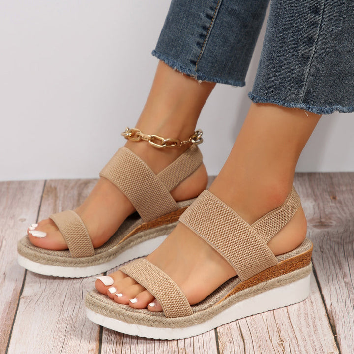Foot model showing front view sandals on khaki floor background.