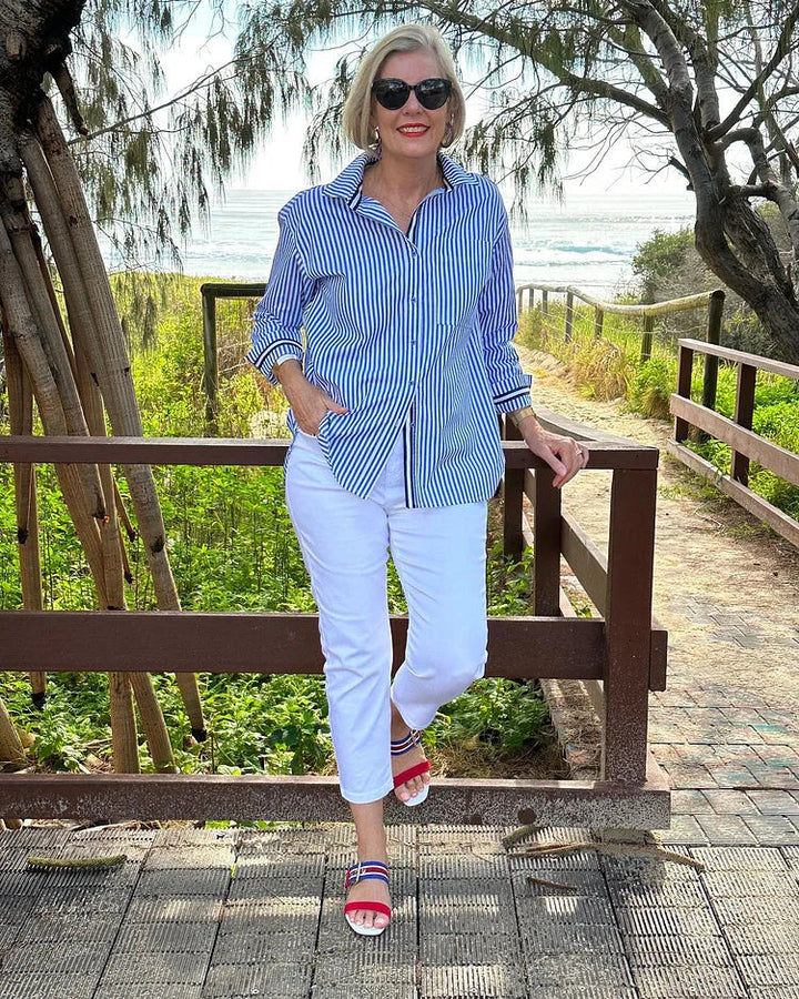 Woman model styled in a relaxed striped shirt against a nature background.