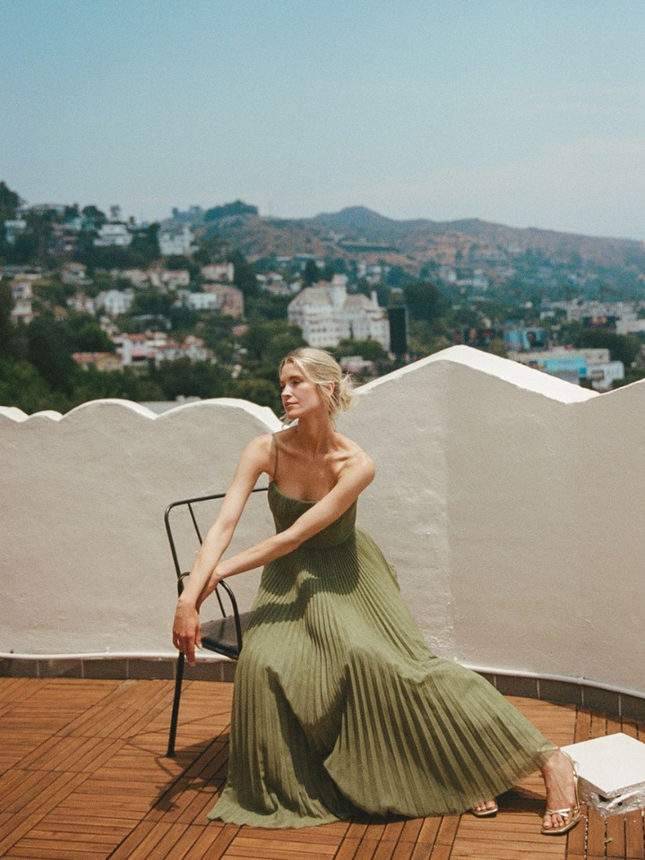 Woman in a dressy pleated outfit standing on a simple plain background.