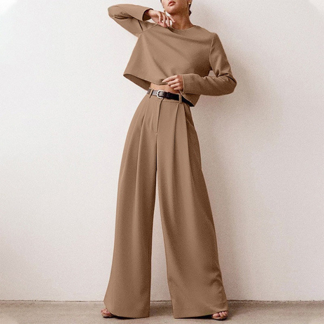 Female model presenting a long-sleeve crop top paired with flowing trousers on a plain background.