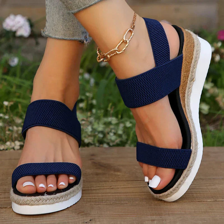 Foot model in casual summer sandals against brown floor.