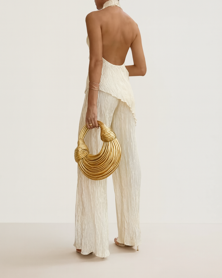 Woman in a black pleated open-back top and wide-leg trousers on a plain background.